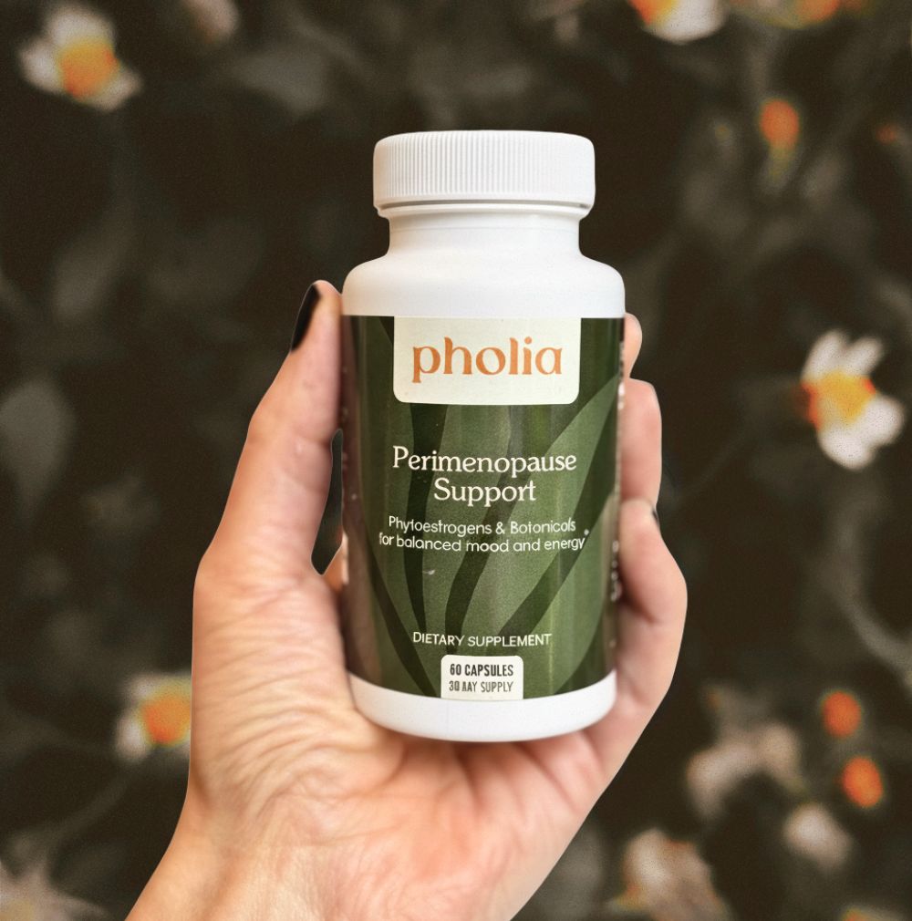 Hand holding a bottle of Pholia Perimenopause Support supplement with a blurred natural background.